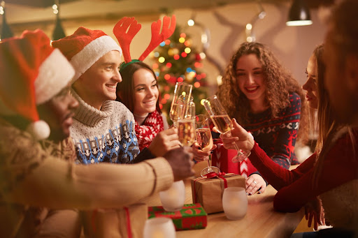 smiling people in christmas clothing clinking champagne glasses and smiling
