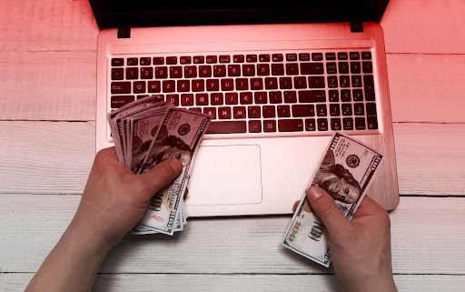hands holding cash over laptop