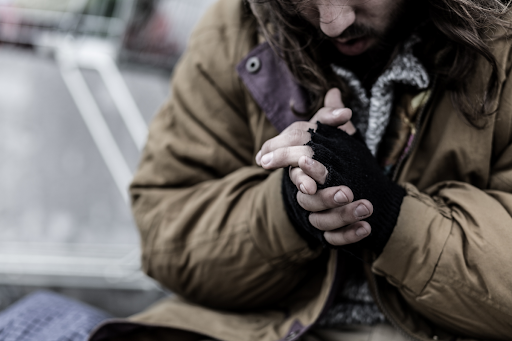 man in coat and fingerless gloves holding hands together for warmth